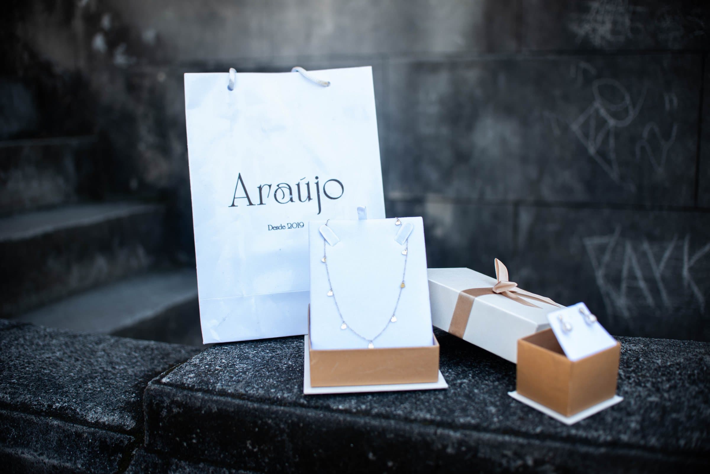 Sacola e caixas de presente Araujo com um colar, sobre pedra escura